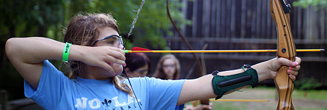 Girl aiming bow and arrow at archery camp activity