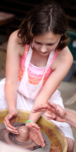 Girl learning to throw pottery on wheel