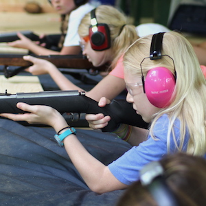 Blond girl shooting rifle at summer camp