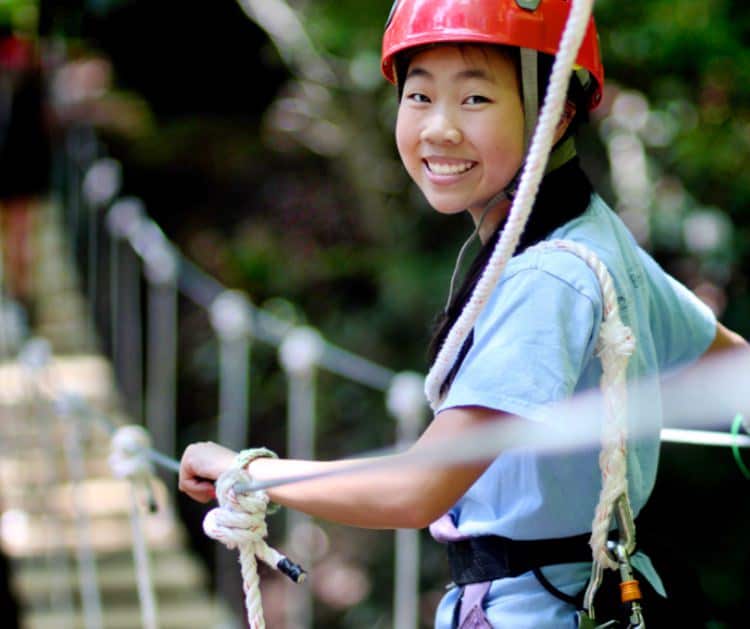 smiling camp girl crossing canopy bridge
