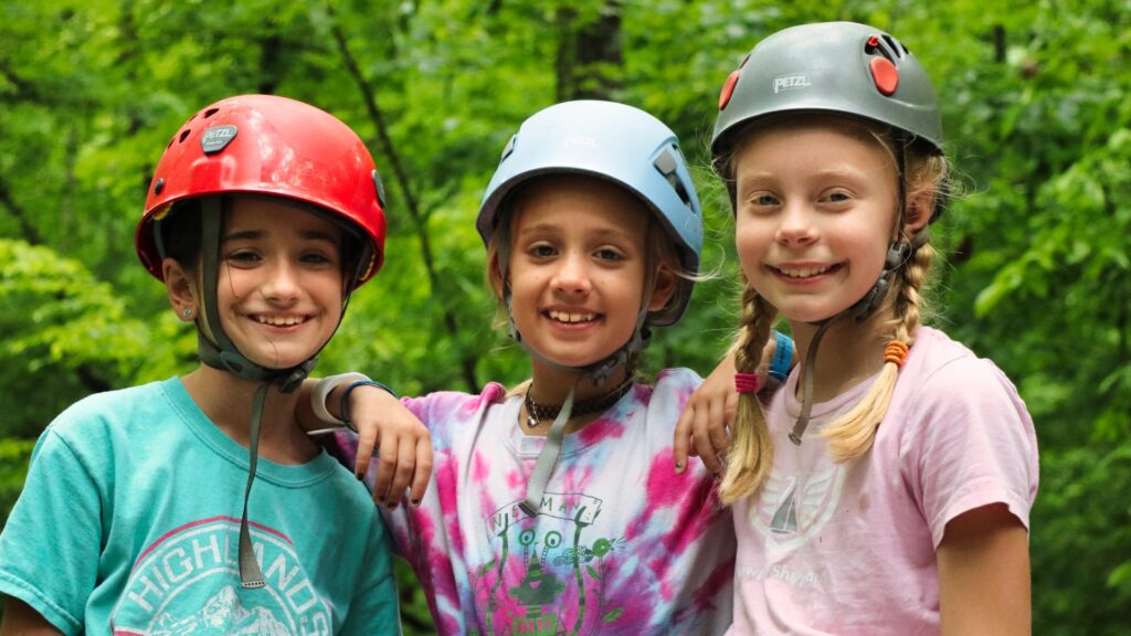 three young teenage camp girls wearing climbing helmets